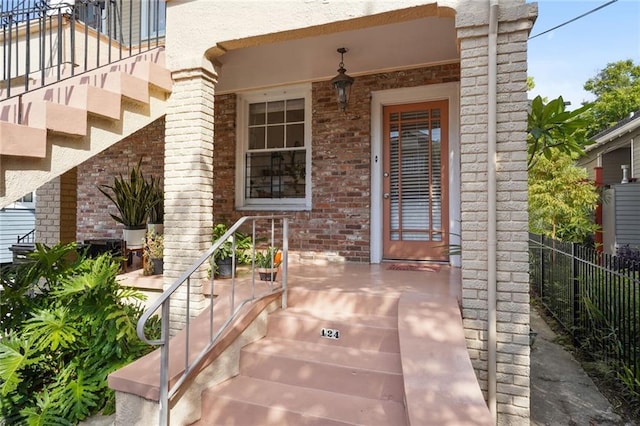 view of exterior entry with brick siding, a porch, and fence