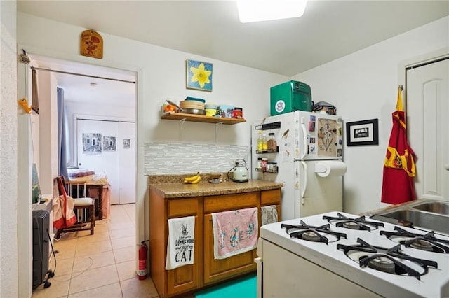 kitchen with light tile patterned floors, white appliances, a sink, decorative backsplash, and brown cabinets