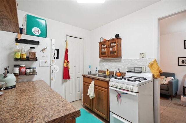 kitchen with white appliances, light tile patterned floors, brown cabinetry, backsplash, and a sink