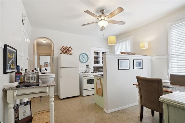 kitchen featuring a wealth of natural light, arched walkways, white appliances, and light floors