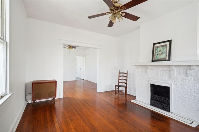 unfurnished living room with ceiling fan, a brick fireplace, wood finished floors, and baseboards