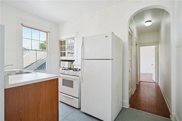 kitchen with arched walkways, white appliances, light countertops, and a sink