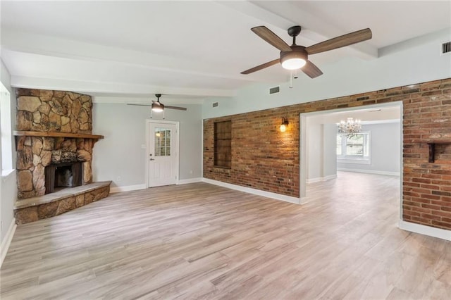 unfurnished living room with a fireplace, brick wall, ceiling fan with notable chandelier, beamed ceiling, and light hardwood / wood-style floors