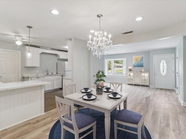 dining room with sink, ceiling fan with notable chandelier, and light wood-type flooring