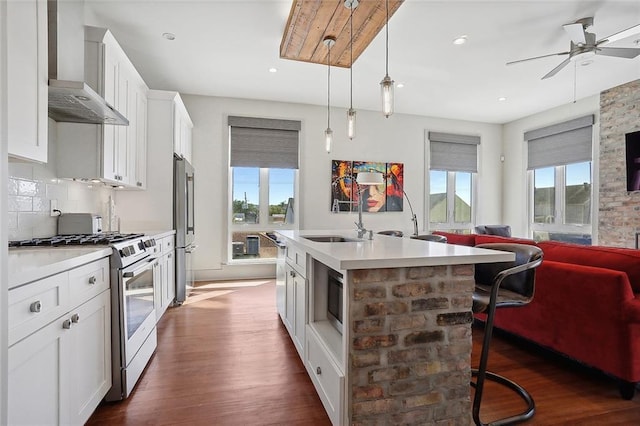 kitchen with premium appliances, wall chimney range hood, pendant lighting, a center island with sink, and white cabinets