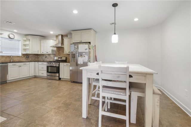 kitchen with wall chimney range hood, sink, hanging light fixtures, decorative backsplash, and appliances with stainless steel finishes