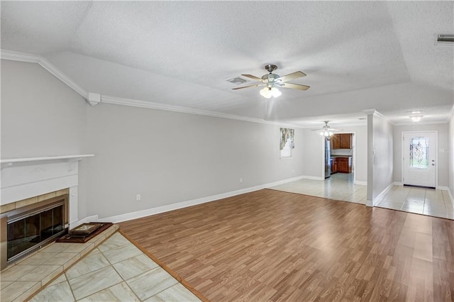 unfurnished living room featuring light wood-type flooring, a textured ceiling, ceiling fan, a tile fireplace, and lofted ceiling