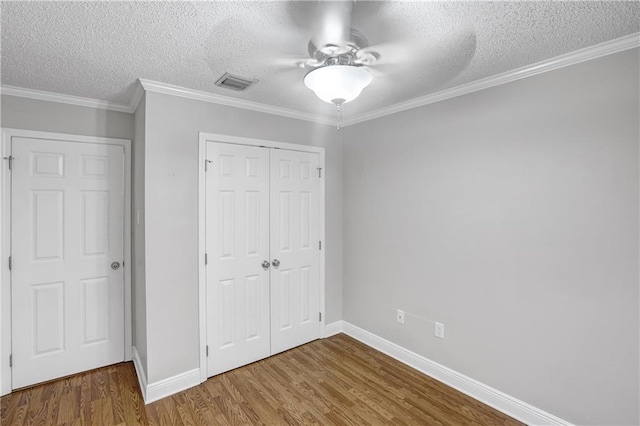 unfurnished bedroom with ceiling fan, ornamental molding, a textured ceiling, wood-type flooring, and a closet