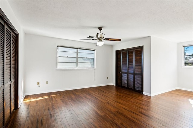 unfurnished bedroom featuring a textured ceiling, dark hardwood / wood-style floors, ceiling fan, and multiple closets