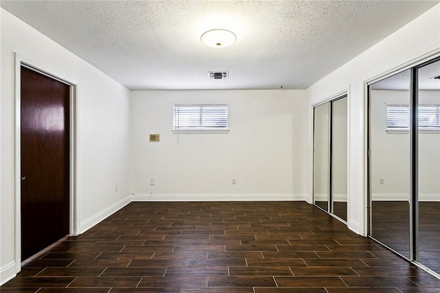 unfurnished bedroom featuring a textured ceiling and multiple closets