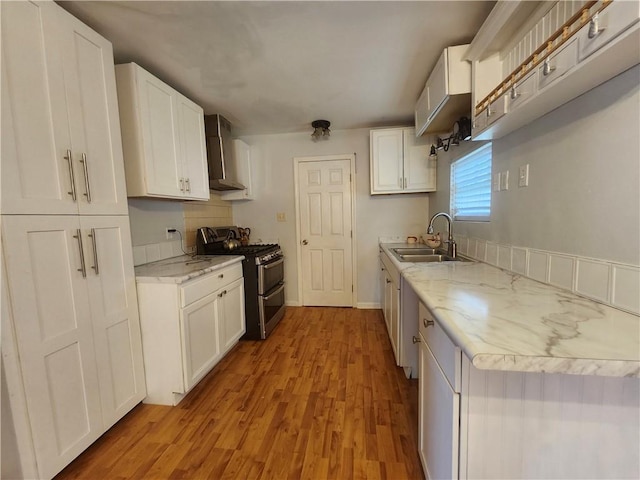 kitchen with wall chimney range hood, gas range, white cabinetry, and sink