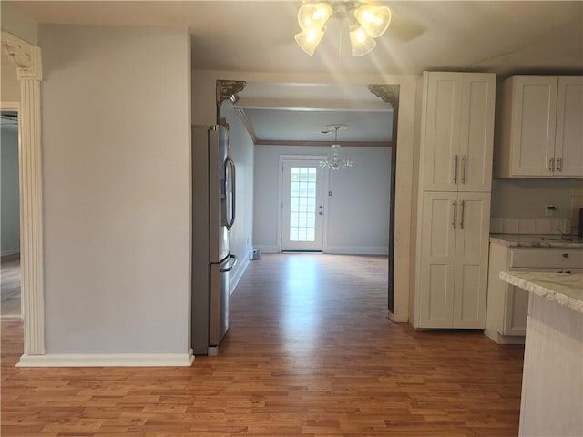 kitchen with hanging light fixtures, stainless steel fridge with ice dispenser, light wood-type flooring, white cabinetry, and a chandelier