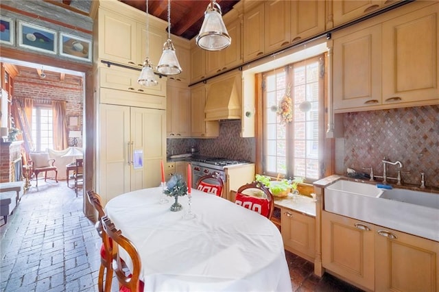 kitchen featuring pendant lighting, custom range hood, sink, high end stainless steel range oven, and brick wall