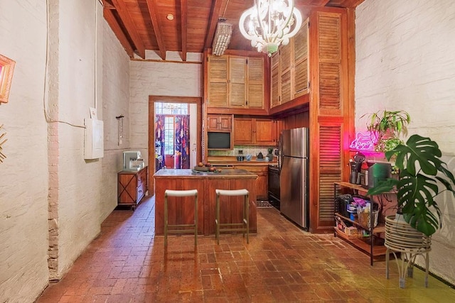 kitchen featuring hanging light fixtures, a towering ceiling, a center island, a breakfast bar, and stainless steel refrigerator