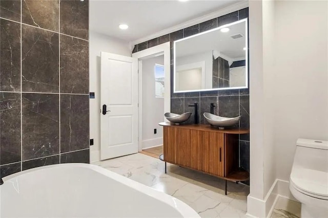 bathroom with a tub, vanity, tile walls, and toilet