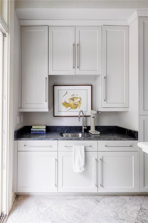 bar featuring dark stone countertops, white cabinetry, and sink