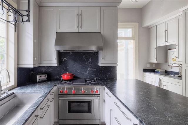 kitchen with luxury stove, white cabinetry, wall chimney exhaust hood, and sink