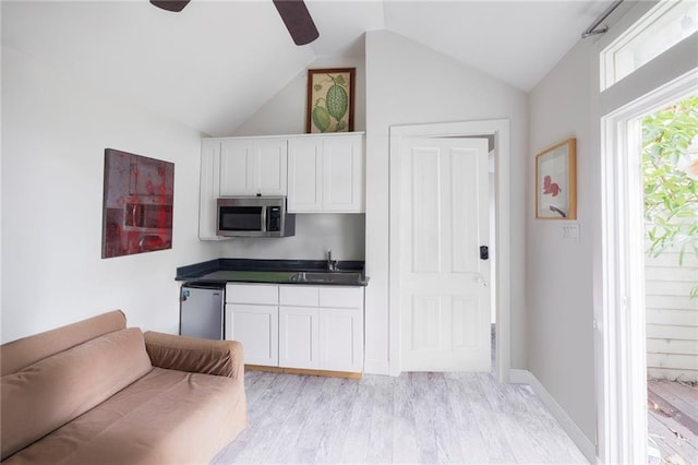 kitchen with light wood-type flooring, vaulted ceiling, ceiling fan, sink, and white cabinetry