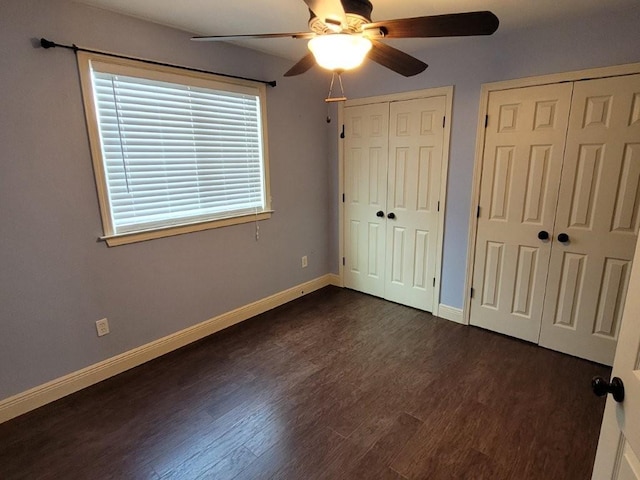 unfurnished bedroom with ceiling fan, dark hardwood / wood-style flooring, and two closets