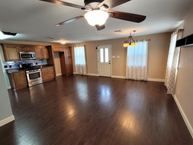 kitchen with ceiling fan with notable chandelier, decorative backsplash, appliances with stainless steel finishes, decorative light fixtures, and dark hardwood / wood-style flooring