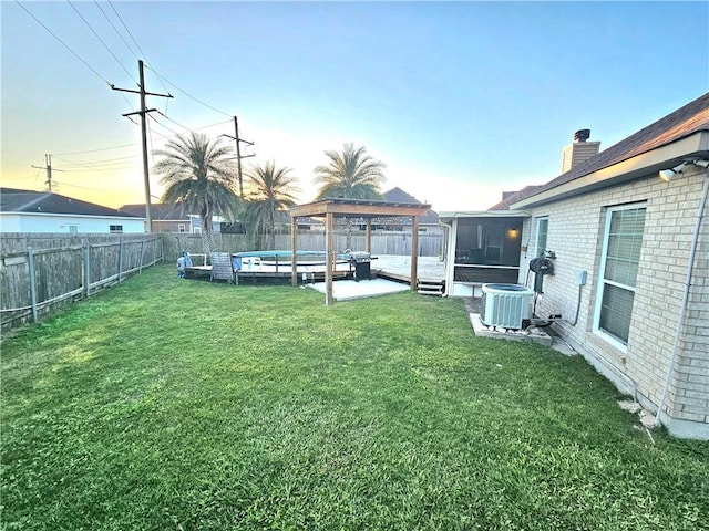 yard at dusk with a pool side deck, a gazebo, central AC unit, and a sunroom