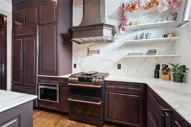 kitchen with high quality appliances, backsplash, light wood-type flooring, light stone counters, and custom range hood