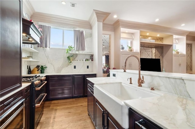 kitchen featuring exhaust hood, sink, tasteful backsplash, light hardwood / wood-style floors, and black range with gas cooktop