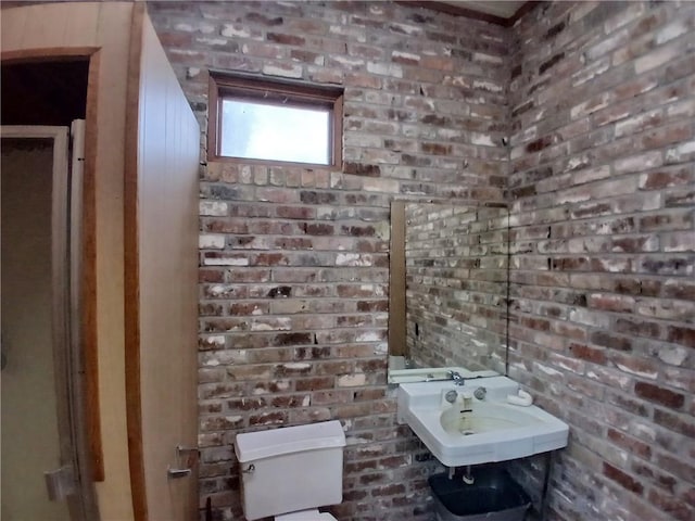 bathroom with sink, toilet, and brick wall