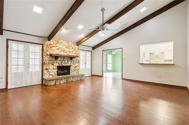 unfurnished living room featuring french doors, ceiling fan, wood-type flooring, a fireplace, and vaulted ceiling with beams