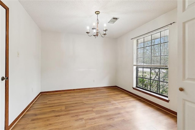 empty room featuring a textured ceiling, light wood-type flooring, and an inviting chandelier