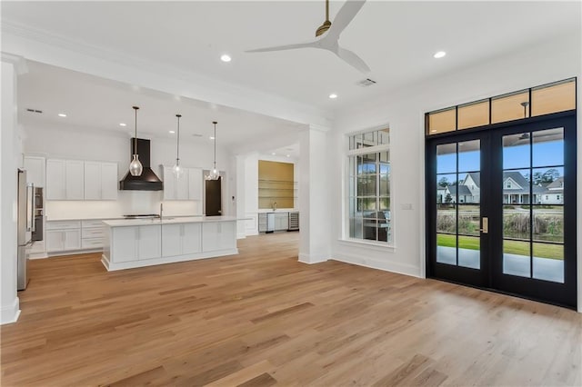 kitchen with pendant lighting, custom exhaust hood, a kitchen island with sink, french doors, and white cabinetry