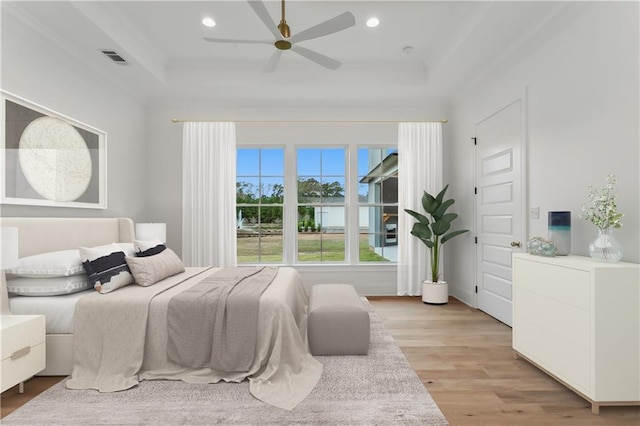 bedroom with light hardwood / wood-style flooring, a raised ceiling, and ceiling fan