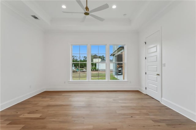 empty room featuring ceiling fan, light wood-type flooring, and a tray ceiling