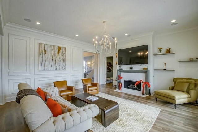 living area featuring stairs, a chandelier, wood finished floors, a decorative wall, and ornamental molding