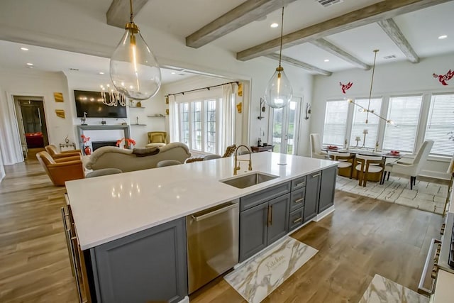 kitchen with a center island with sink, gray cabinets, pendant lighting, stainless steel dishwasher, and sink