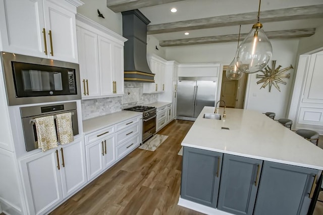 kitchen featuring beam ceiling, decorative backsplash, sink, built in appliances, and white cabinetry