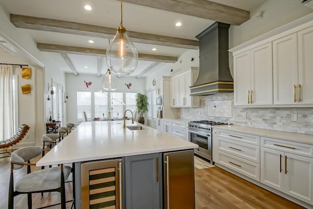 kitchen featuring beverage cooler, high end range, an island with sink, a breakfast bar, and custom range hood