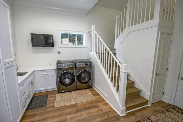 laundry room with wood finished floors, washing machine and clothes dryer, cabinet space, and a sink