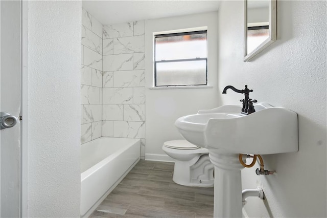 bathroom with hardwood / wood-style floors, toilet, and tiled shower / bath