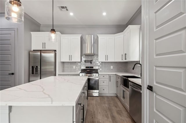 kitchen featuring wall chimney range hood, pendant lighting, sink, appliances with stainless steel finishes, and white cabinets