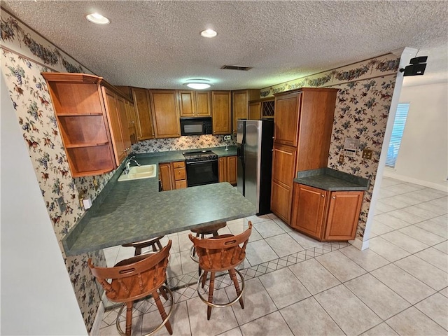 kitchen with sink, kitchen peninsula, a textured ceiling, light tile patterned floors, and black appliances