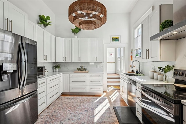 kitchen featuring appliances with stainless steel finishes, white cabinetry, wall chimney exhaust hood, and sink