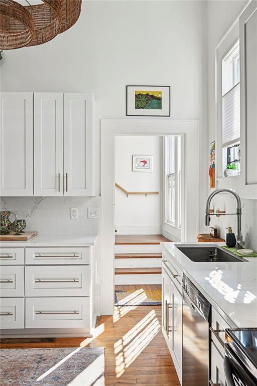 kitchen with light stone counters, stainless steel dishwasher, sink, light hardwood / wood-style flooring, and white cabinets