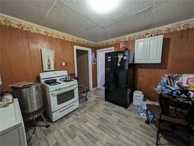 kitchen featuring a textured ceiling, white range with gas cooktop, wooden walls, light hardwood / wood-style floors, and black fridge