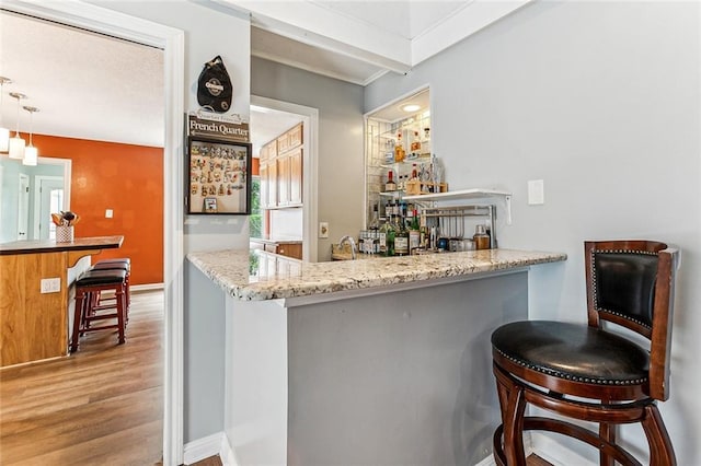 bar featuring beamed ceiling, light hardwood / wood-style floors, light stone countertops, and hanging light fixtures