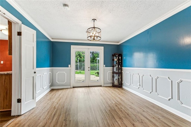 spare room featuring french doors, an inviting chandelier, crown molding, light hardwood / wood-style floors, and a textured ceiling