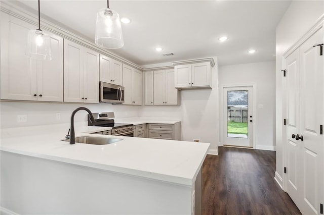 kitchen featuring decorative light fixtures, kitchen peninsula, sink, dark wood-type flooring, and stainless steel appliances