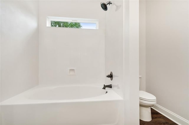 bathroom with hardwood / wood-style flooring, washtub / shower combination, and toilet