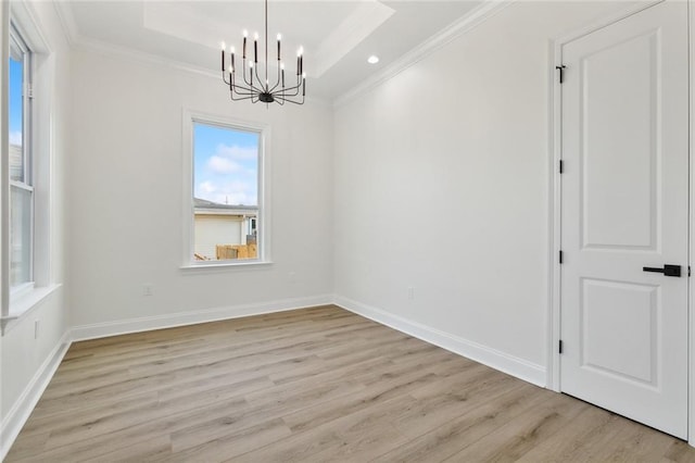 spare room with a tray ceiling, ornamental molding, a chandelier, and light wood-type flooring