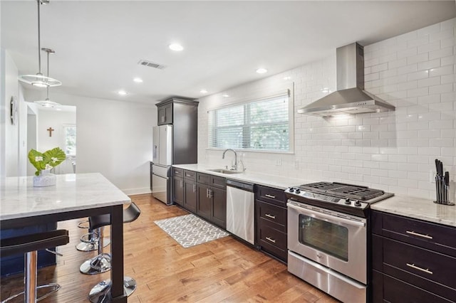 kitchen with sink, wall chimney exhaust hood, tasteful backsplash, decorative light fixtures, and appliances with stainless steel finishes